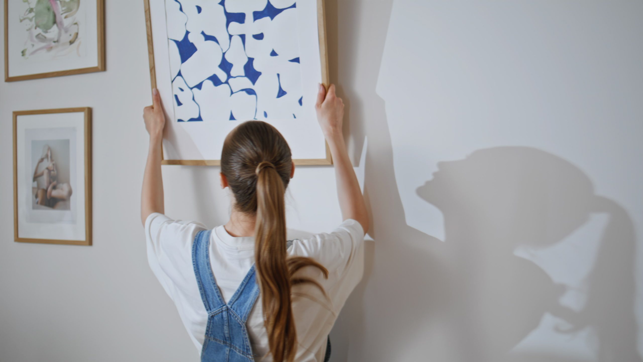 Girl hanging art picture on canvas at modern apartment during relocation closeup